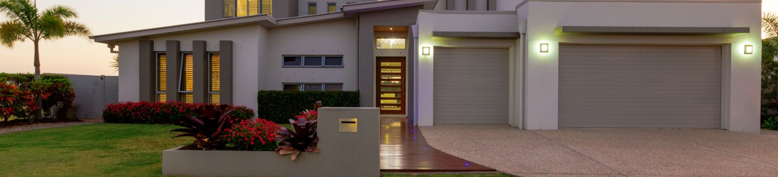 Modern Home Exterior with Double Garage Doors at Sunset in Alpine, CA Contemporary Alpine home with well-lit double garage doors and landscaped yard, representing top-rated garage door and gate services in Alpine, California.